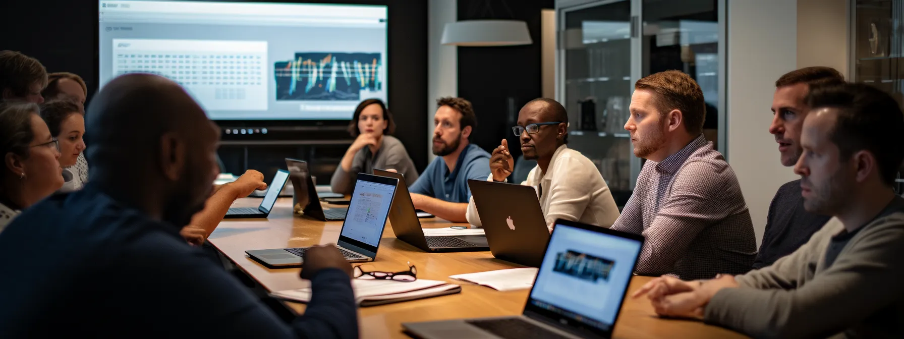 a group of individuals sitting in a classroom-like setting, focused on a computer screen displaying seo tools and analytics platforms while engaging in discussion.
