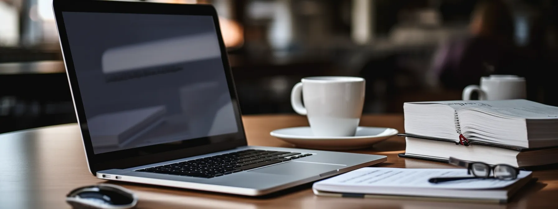 a person holding a stack of seo books with a laptop open on a table, surrounded by a pen, notebook, and coffee cup.